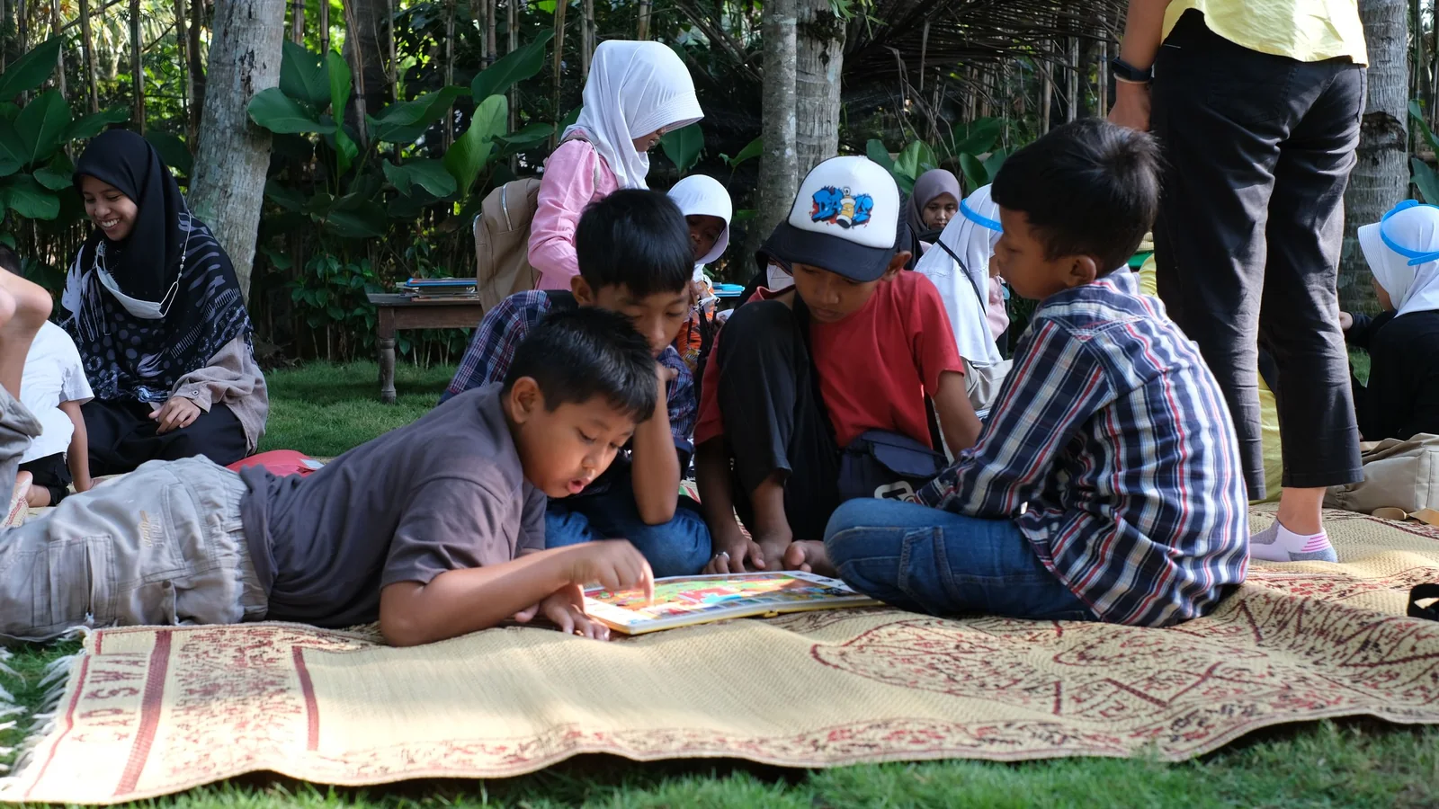 Niñas y niños leyendo juntos al aire libre durante una actividad recreativa.