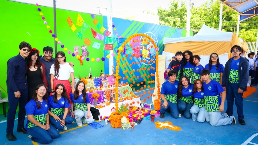 Estudiantes de Bachillerato de Colegio Latino con maquillaje de Catrina junto a una ofrenda de Día de Muertos