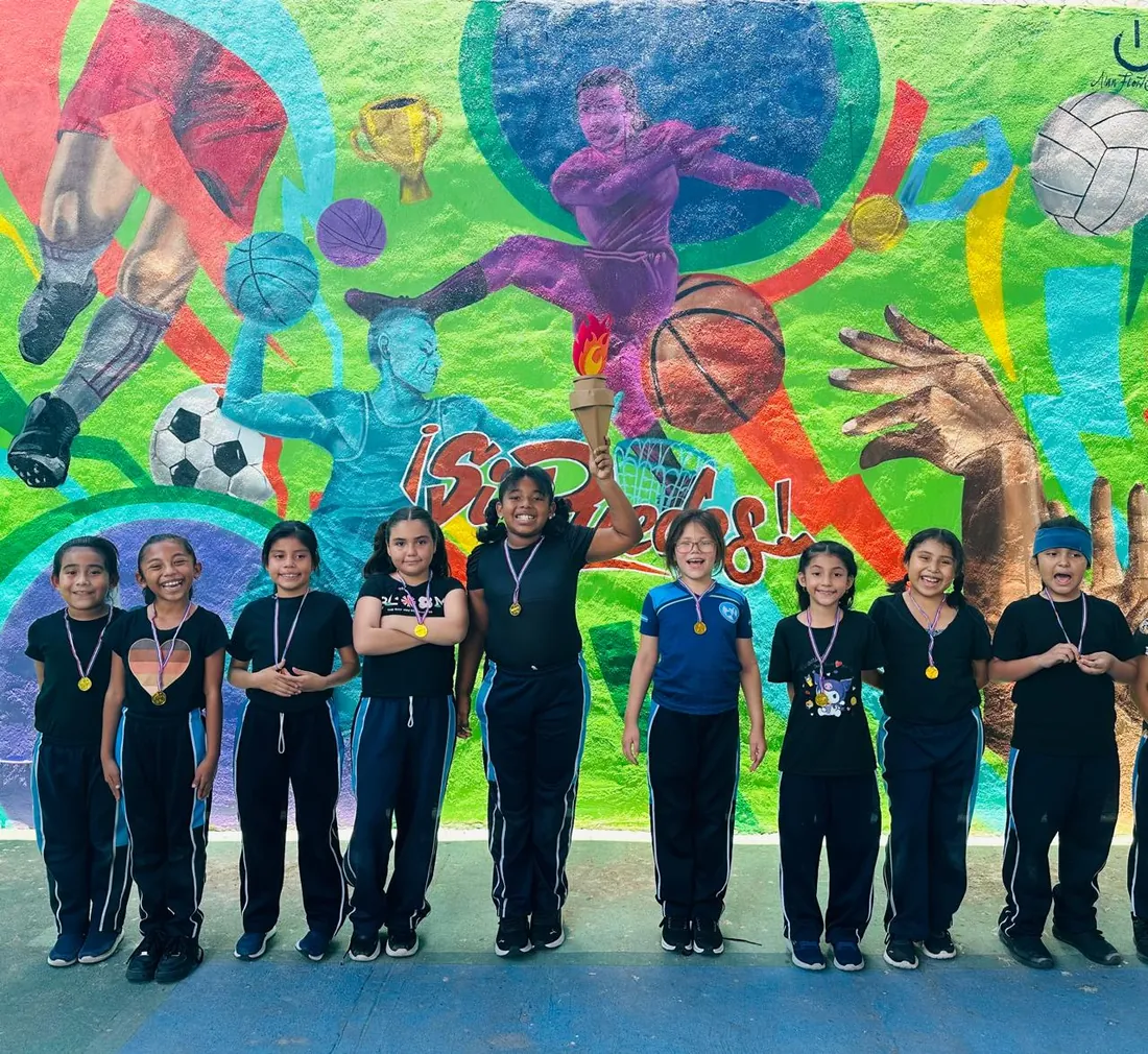 Equipo de Primaria de Colegio Latino con medallas frente a un mural deportivo