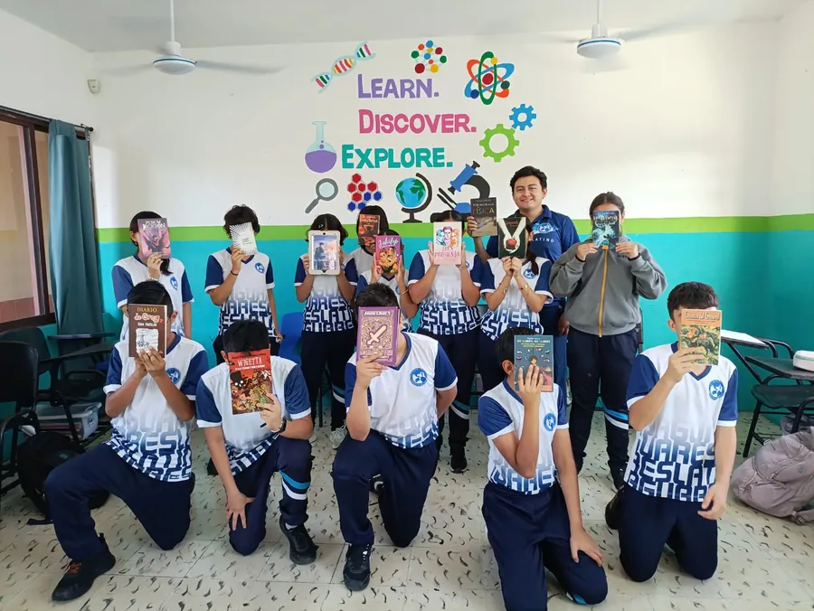 Estudiantes de Secundaria de Colegio Latino mostrando libros frente a un mural sobre ciencia y lectura