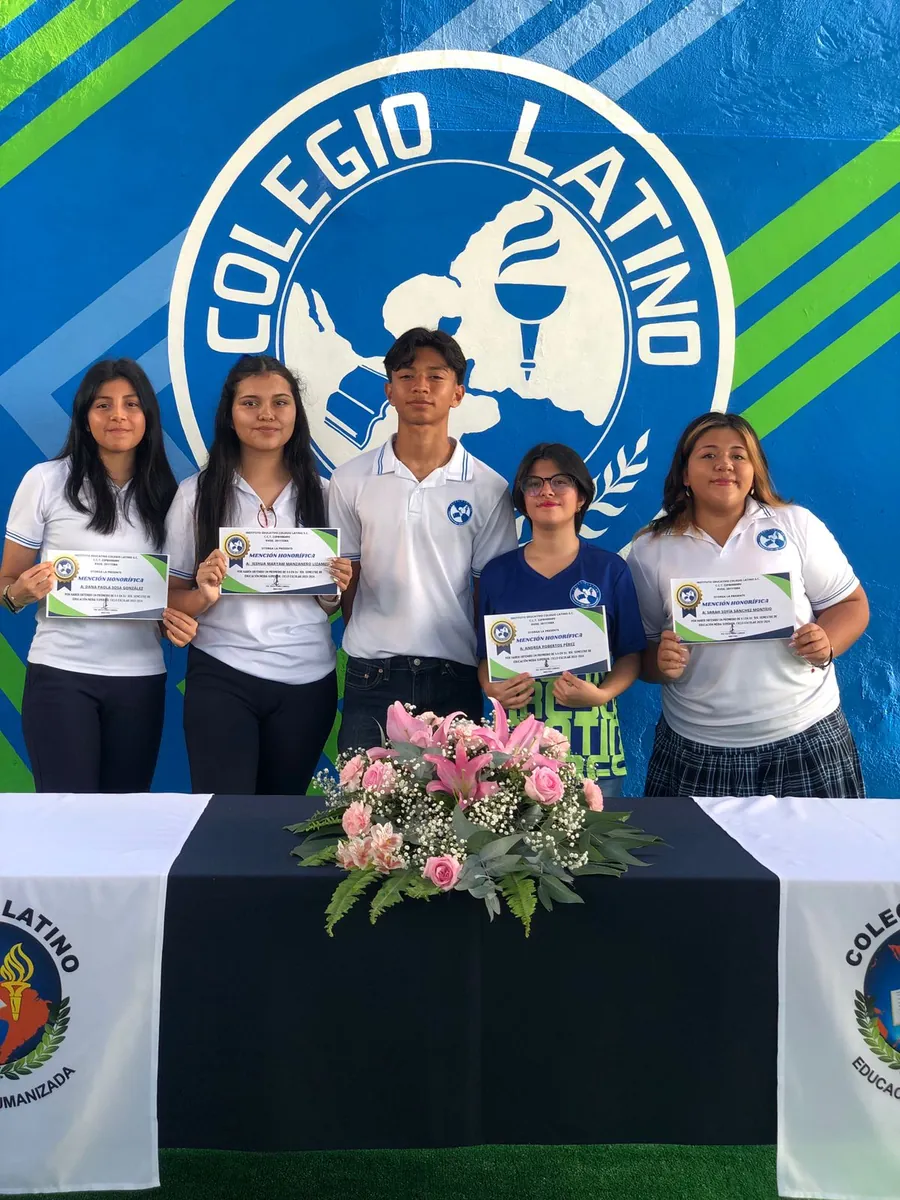 Estudiantes de Colegio Latino recibiendo un reconocimiento por mención honorífica frente al emblema institucional